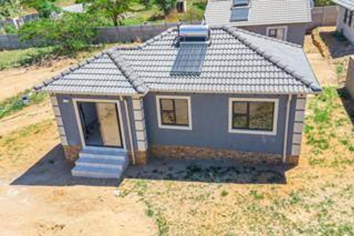 Aerial view of a modern single-story house featuring a tiled roof with a solar water heater, stone cladding accents, and a sliding glass door entrance.