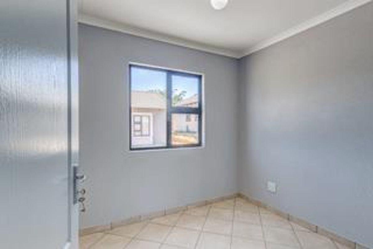 A clean, empty bedroom featuring neutral grey walls, tiled flooring, and an aluminium-framed window, providing a blank canvas for personalization.