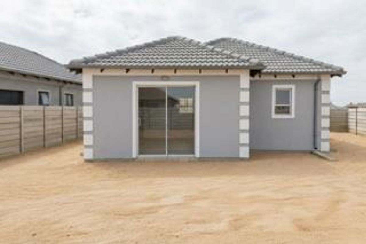Rear view of a modern single-story house featuring a tiled roof, sliding glass door, and a surrounding precast concrete boundary wall.