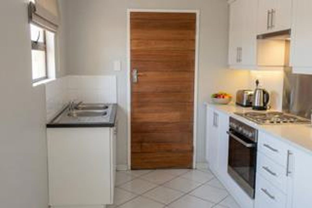 Modern kitchen featuring white cabinetry, stainless steel appliances, built-in oven, hob, and tiled flooring with a wooden door.