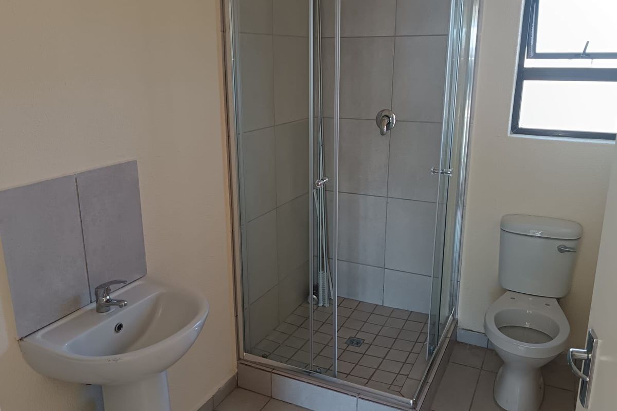 A functional bathroom featuring a pedestal basin, a glass-enclosed shower, and a standard toilet with neutral tiled flooring.