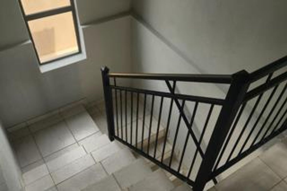 A staircase featuring tiled steps and a black metal balustrade, illuminated by a side window.