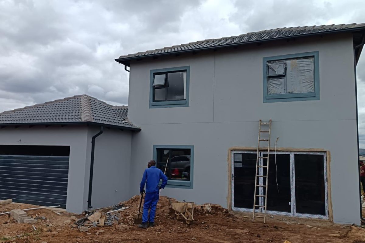 Rear view of a two-story house under construction, featuring grey exterior walls, tiled roofing, and installed aluminium window and door frames.