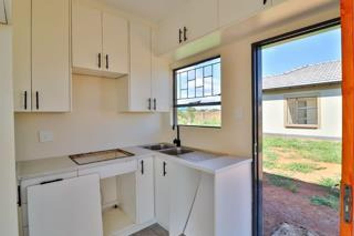 A compact kitchen area featuring white cabinetry, a stainless steel sink, and direct access to the rear yard through a sliding glass door.