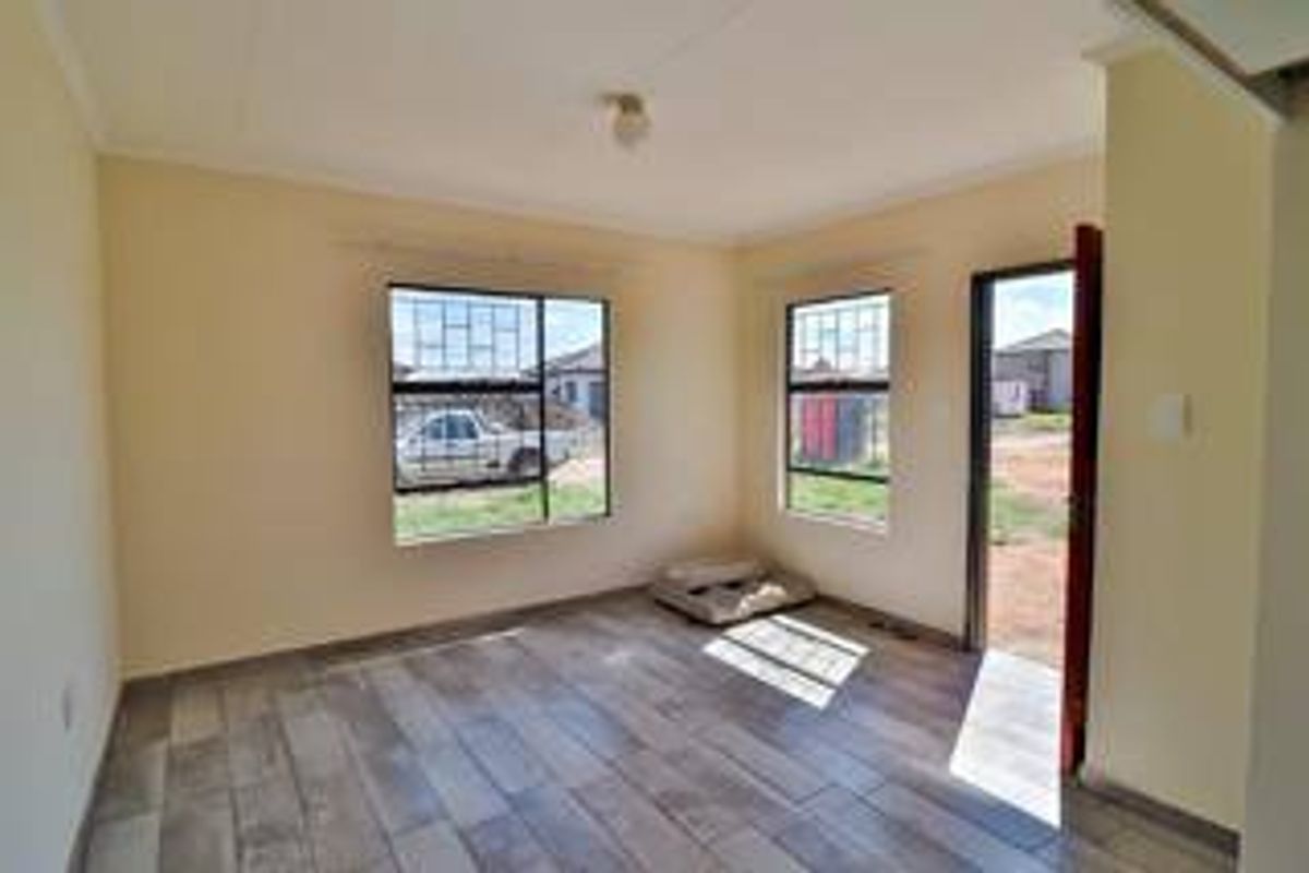 A bright, empty living room featuring tiled flooring, security bars on the windows, and direct access to the exterior.
