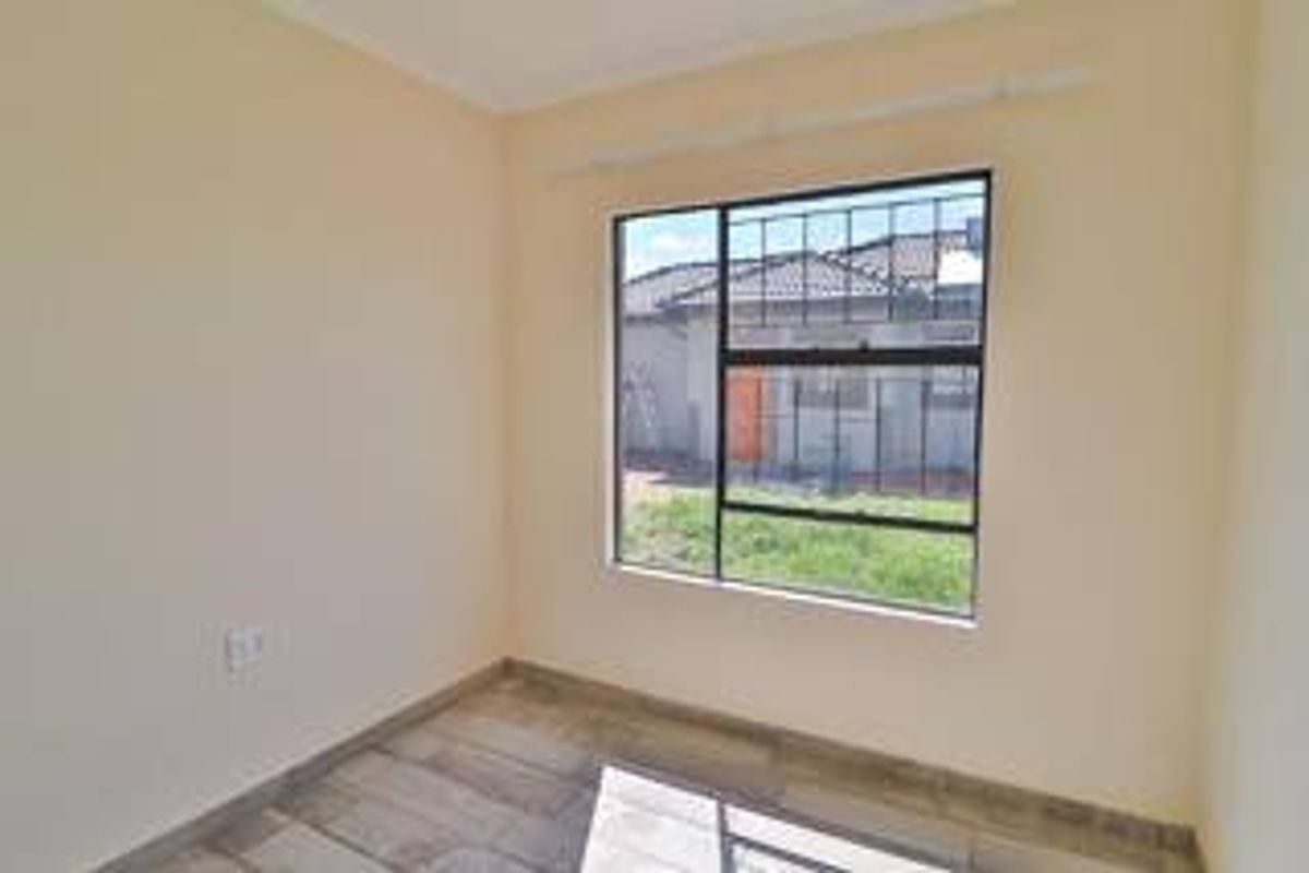 A bright, empty bedroom featuring tiled flooring, neutral walls, and a window fitted with security burglar bars.