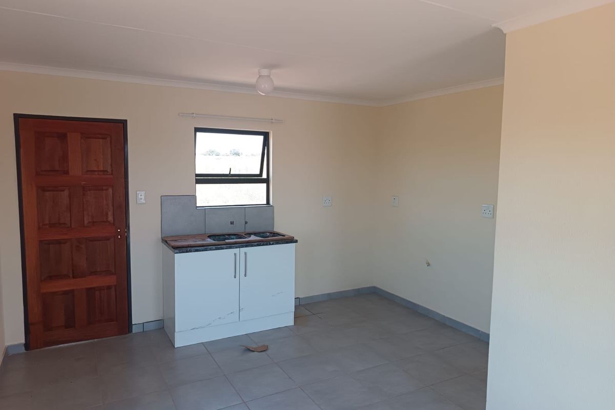 A compact, empty kitchen area featuring tiled flooring, a single base cabinet unit with a sink, and a timber entrance door.