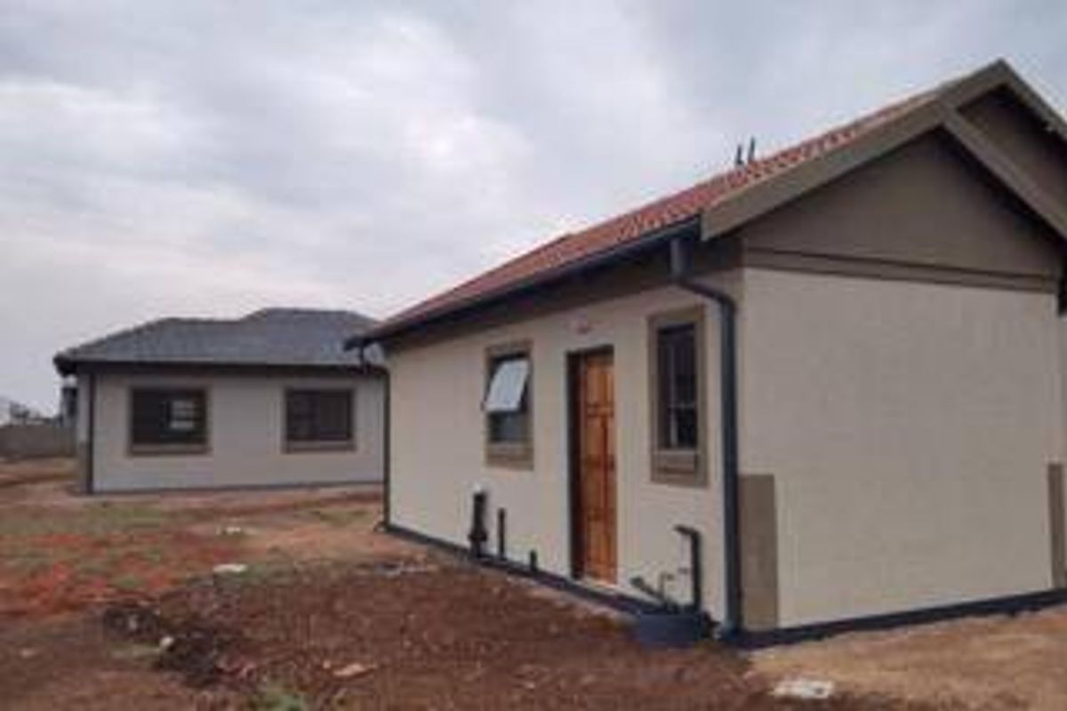 Rear view of a modern single-story residential house featuring plastered walls, a tiled roof, and unfinished surrounding grounds.