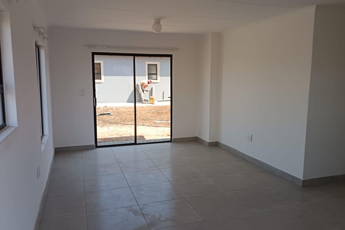 A bright, empty living room featuring neutral tiled flooring, clean white walls, and a sliding glass door providing access to the exterior.