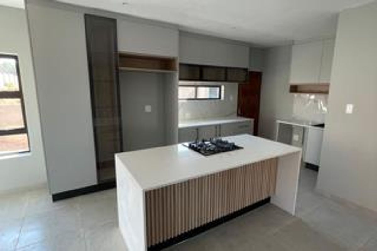 Modern kitchen featuring a central island with a gas hob, sleek built-in cabinetry, stone countertops, and neutral tiled flooring in an open-plan layout.