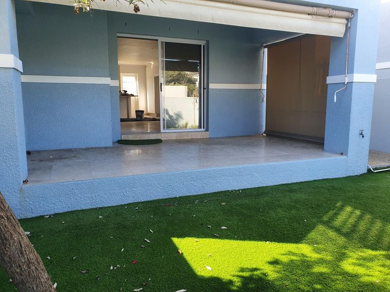 Covered patio area featuring tiled flooring, a retractable awning, and direct access to the interior through a sliding glass door, overlooking a synthetic lawn.