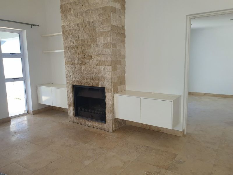 Spacious living area featuring a prominent stone-clad fireplace, built-in floating cabinetry, and neutral stone floor tiles throughout.