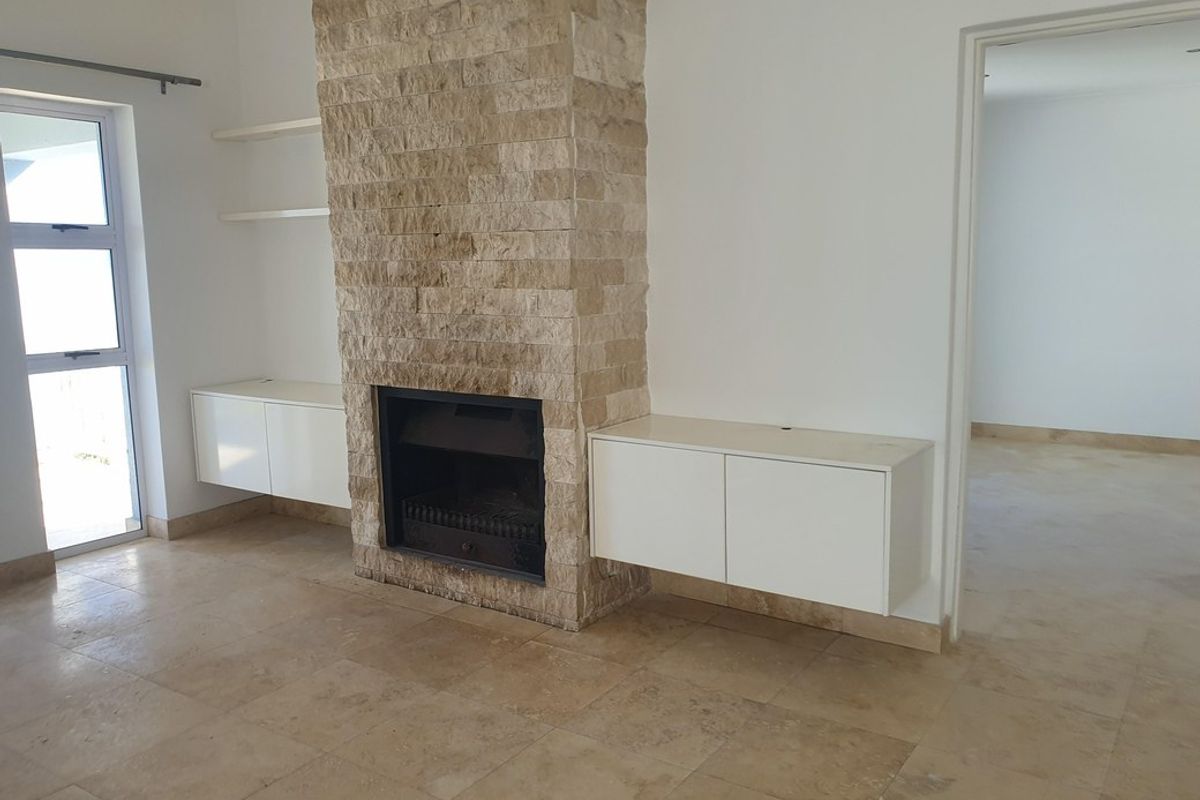 Spacious living area featuring a prominent stone-clad fireplace, built-in floating cabinetry, and neutral stone floor tiles throughout.