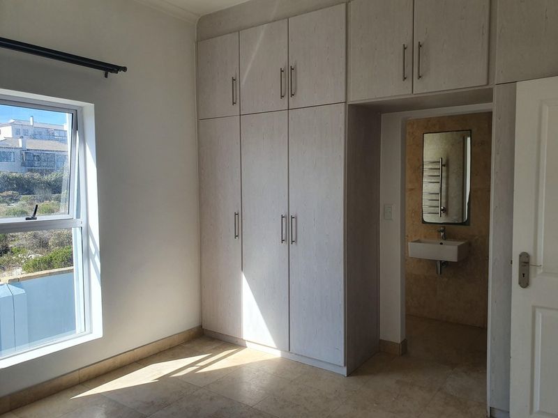 A bright bedroom featuring built-in cupboards and an adjoining en-suite bathroom with a wall-mounted vanity and heated towel rail.