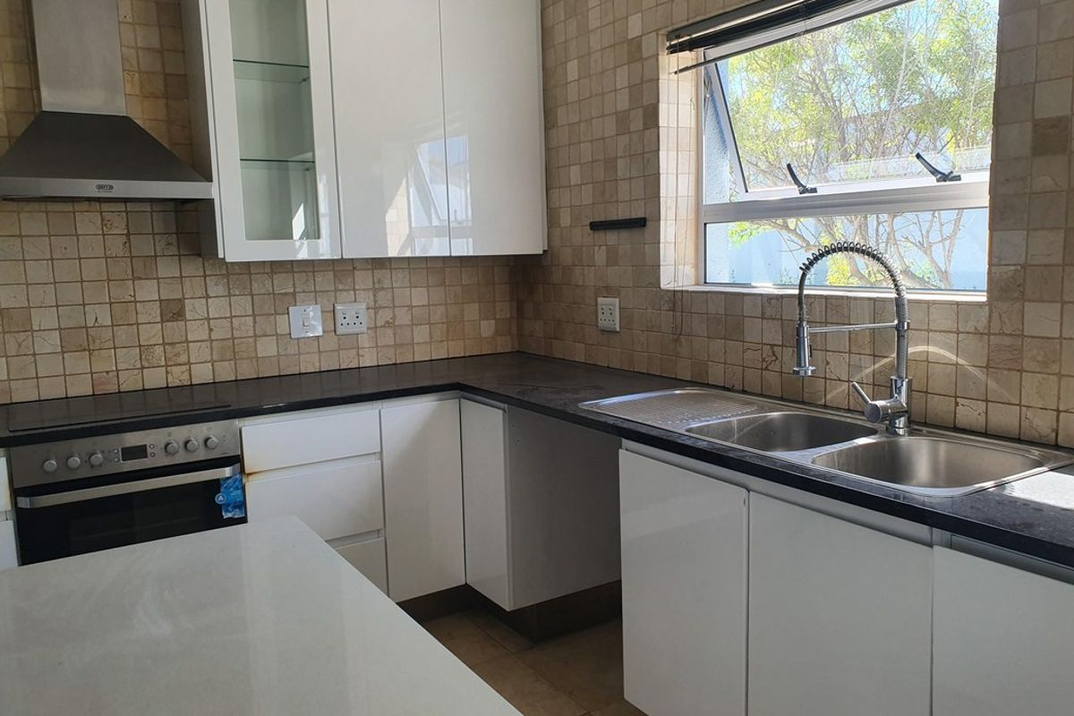A functional kitchen featuring white cabinetry, dark stone countertops, a built-in oven, extractor fan, and a double sink with a modern faucet.