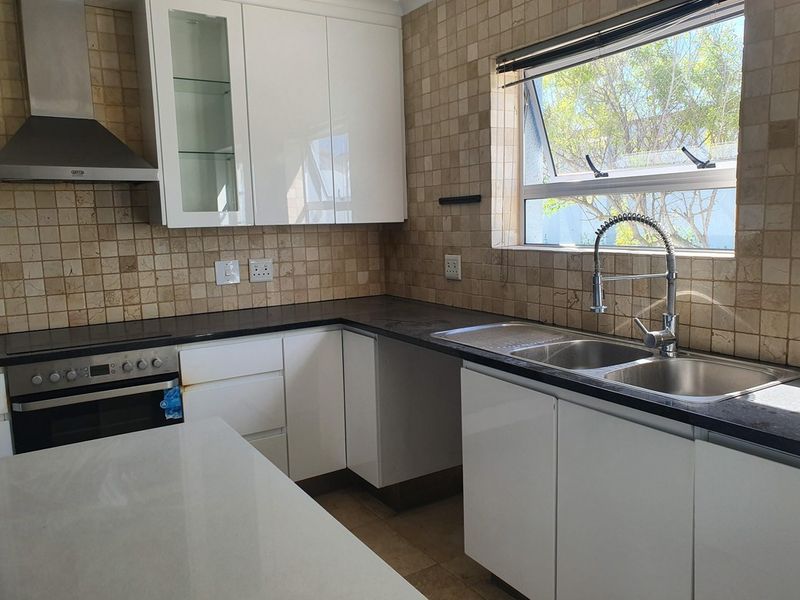 A functional kitchen featuring white cabinetry, dark stone countertops, a built-in oven, extractor fan, and a double sink with a modern faucet.