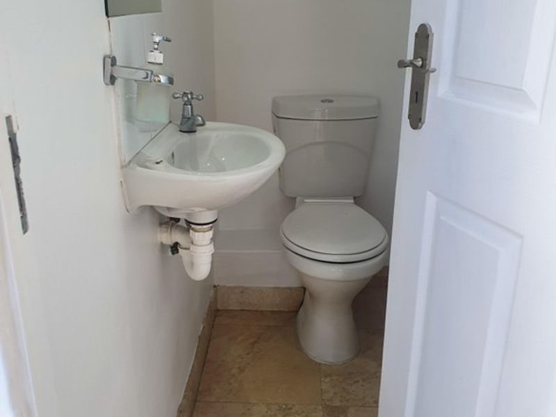 A compact guest bathroom featuring a wall-mounted basin, toilet, and tiled flooring, presenting a functional space in need of minor cosmetic updates.