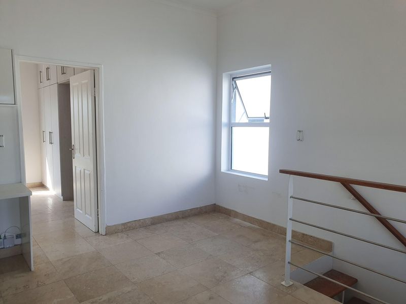 An empty hallway featuring tiled flooring, built-in storage cupboards, and a staircase with a modern metal balustrade and wooden handrail.