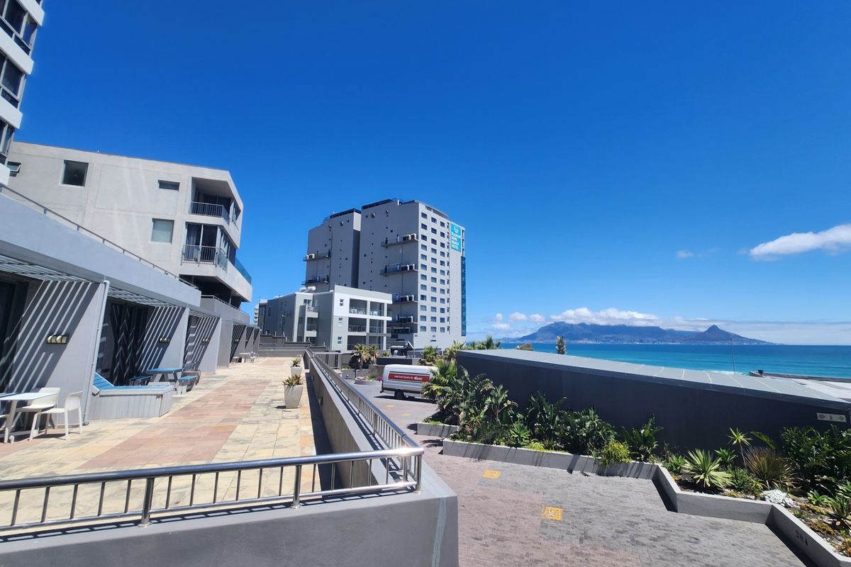 A wide-angle view of the apartment complex exterior, featuring paved walkways, modern building facades, and scenic coastal views.