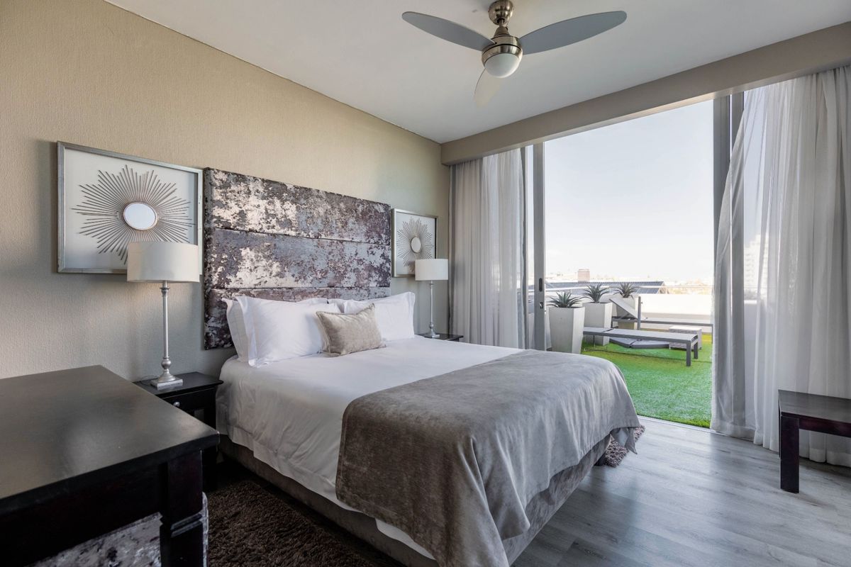 A well-appointed bedroom featuring modern laminate flooring, a ceiling fan, and large sliding glass doors opening onto a private balcony.