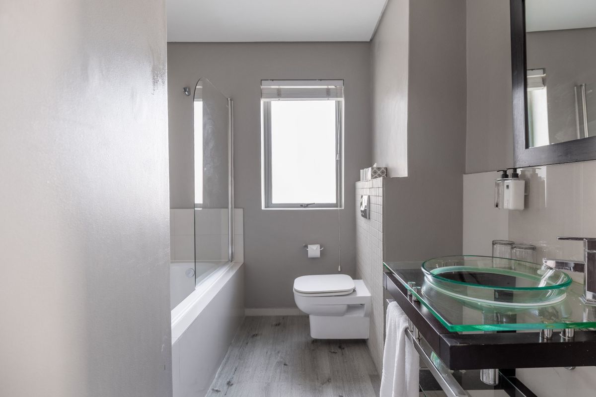 Modern bathroom featuring a wall-mounted toilet, glass vessel sink, and a bathtub with a glass shower screen.