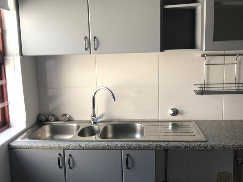 A clean and functional kitchen area featuring grey built-in cabinetry, a double bowl stainless steel sink, and durable granite countertops with tiled splashbacks.
