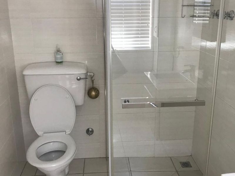 A clean, functional bathroom featuring a glass-enclosed shower, tiled flooring, and wall tiling, providing a bright and neutral space.