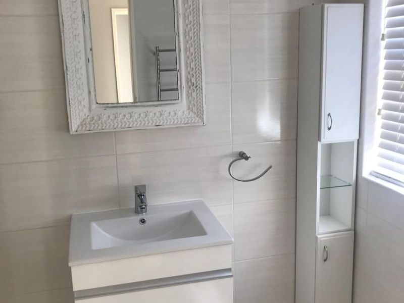 A clean, modern bathroom featuring a wall-mounted vanity with basin, tall storage cabinetry, and neutral wall and floor tiling.