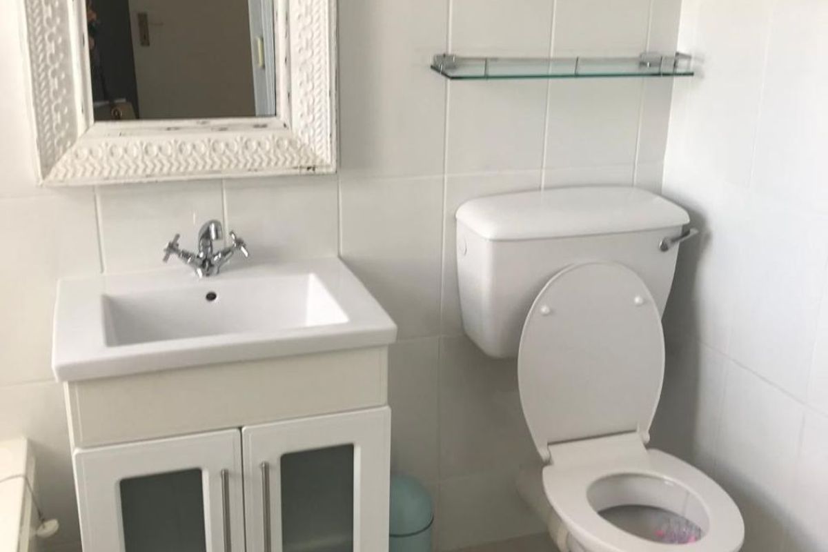 A functional bathroom featuring a white vanity cabinet with a basin, a standard toilet, and neutral wall and floor tiling.