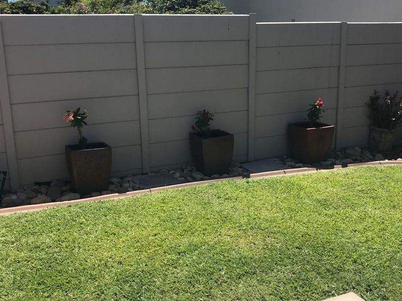 A well-maintained garden area featuring a neat lawn, paved border, and a solid precast concrete boundary wall.