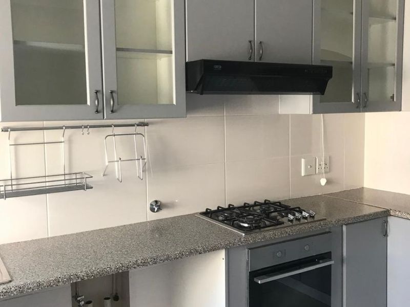 Modern kitchen featuring grey cabinetry, granite countertops, built-in oven, gas hob, and extractor fan with tiled backsplash and flooring.