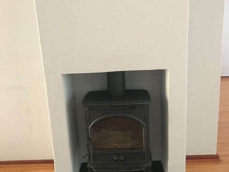 A bright living area featuring a classic cast iron wood burning stove set within a clean white fireplace surround and laminate flooring.