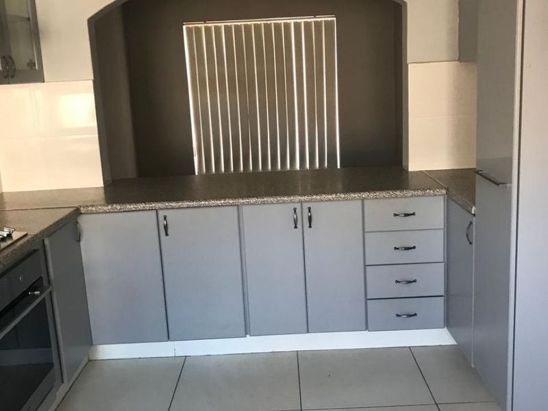 A functional kitchen featuring grey built-in cabinetry, granite countertops, a built-in oven, and tiled flooring with a distinctive arched wall feature.