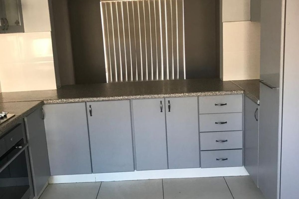 A functional kitchen featuring grey built-in cabinetry, granite countertops, a built-in oven, and tiled flooring with a distinctive arched wall feature.