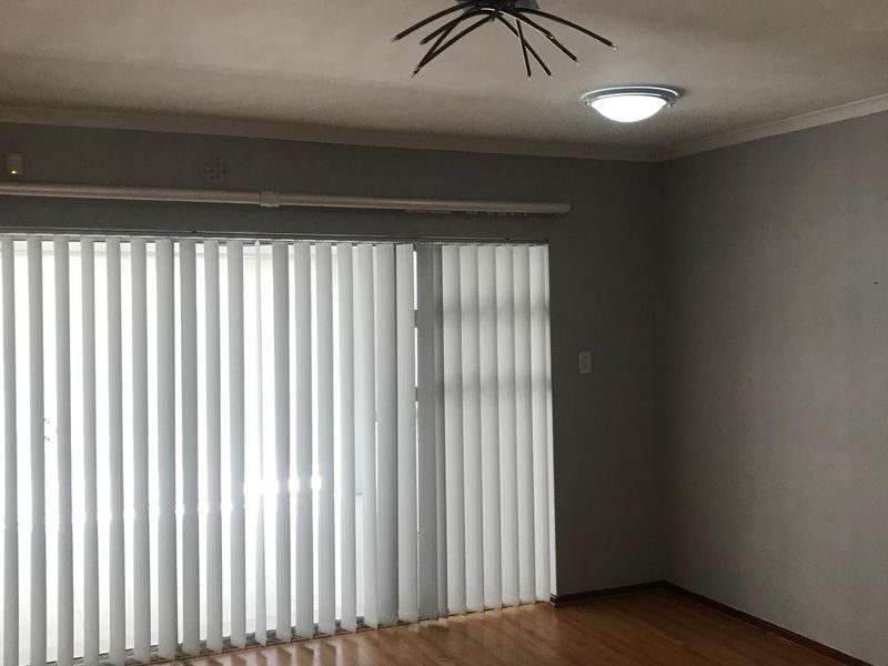An empty living room featuring hardwood flooring, vertical blinds, and a ceiling light fixture.