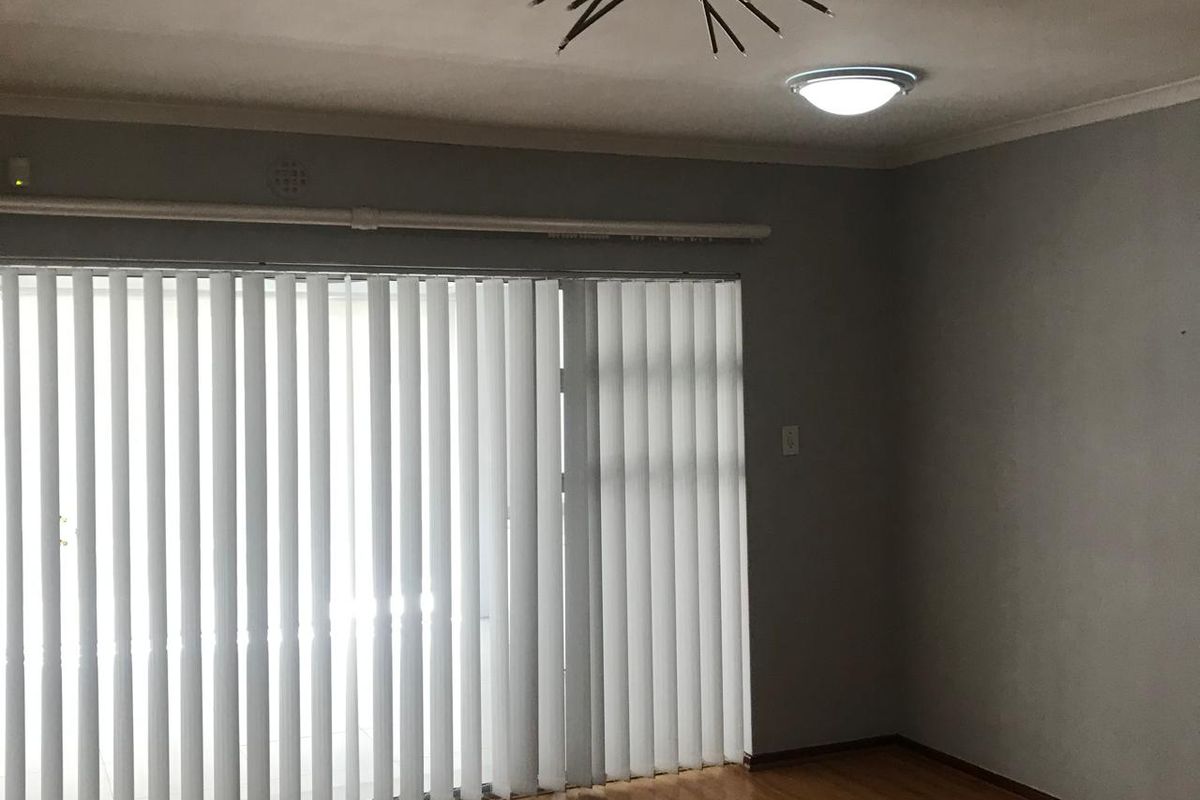 An empty living room featuring hardwood flooring, vertical blinds, and a ceiling light fixture.