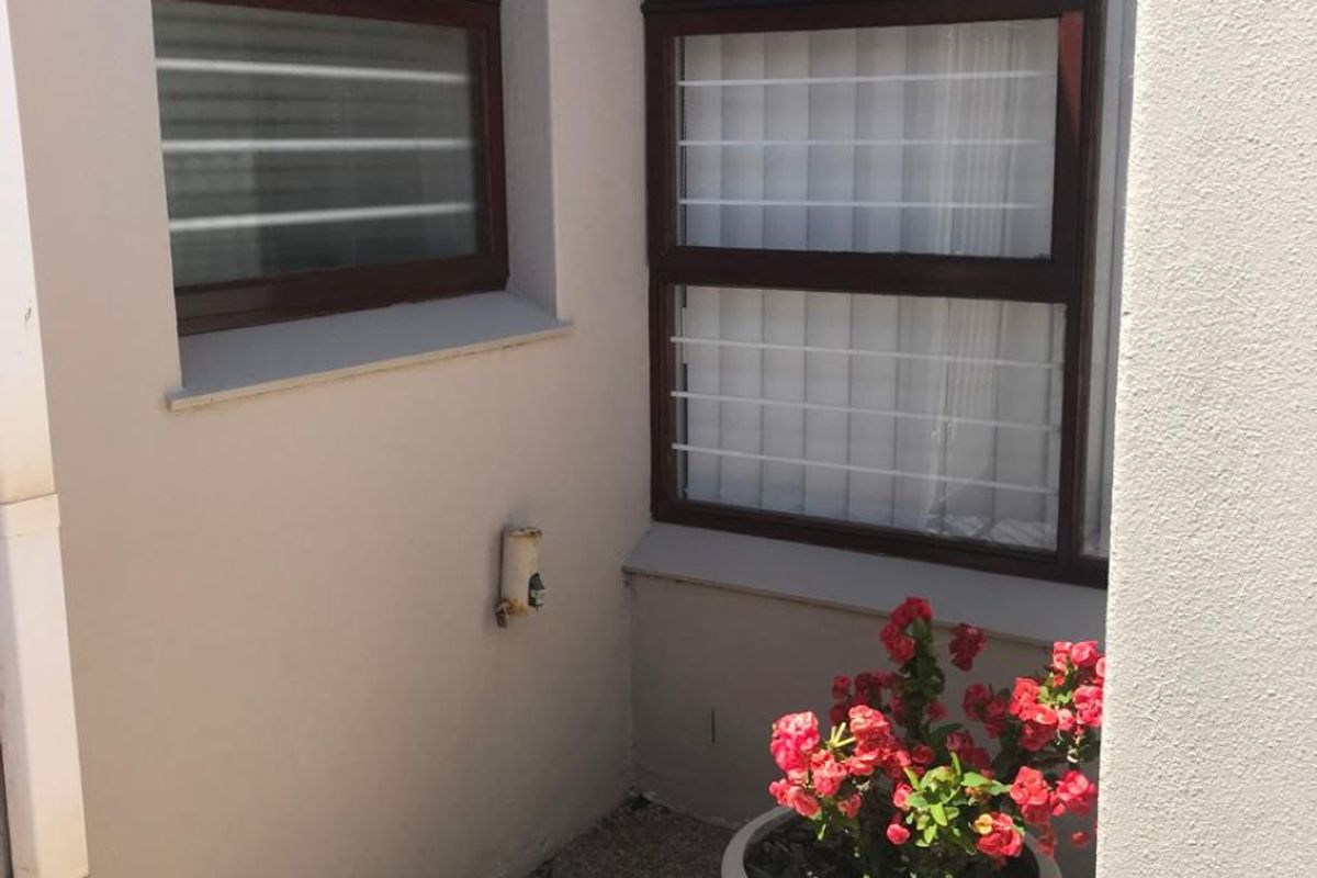 A small, tidy exterior corner area featuring paved flooring, aluminium window frames with security bars, and an external water tap.