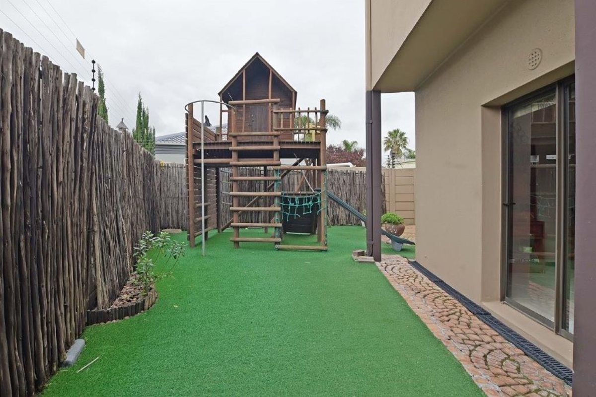 A private rear garden area featuring artificial turf, a wooden boundary fence, and a paved walkway adjacent to the main building structure.