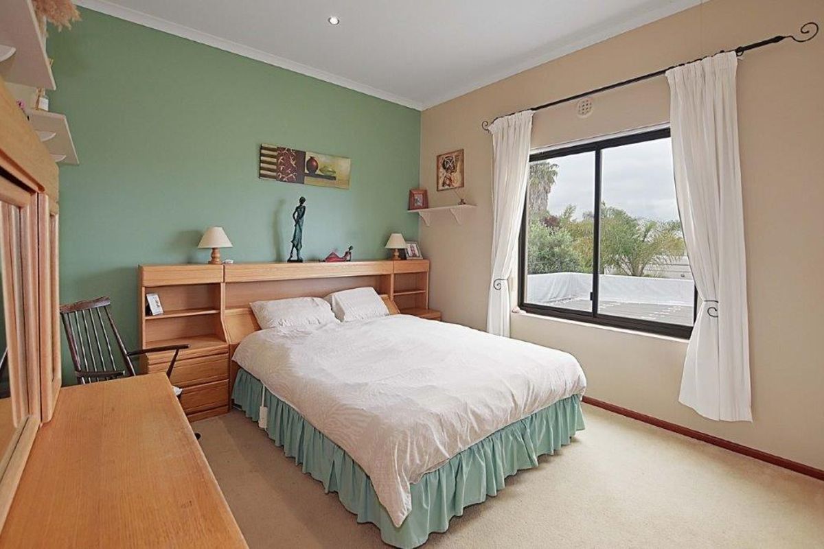 A well-lit bedroom featuring a built-in wooden headboard with integrated shelving, neutral carpeting, and a large window providing natural light.