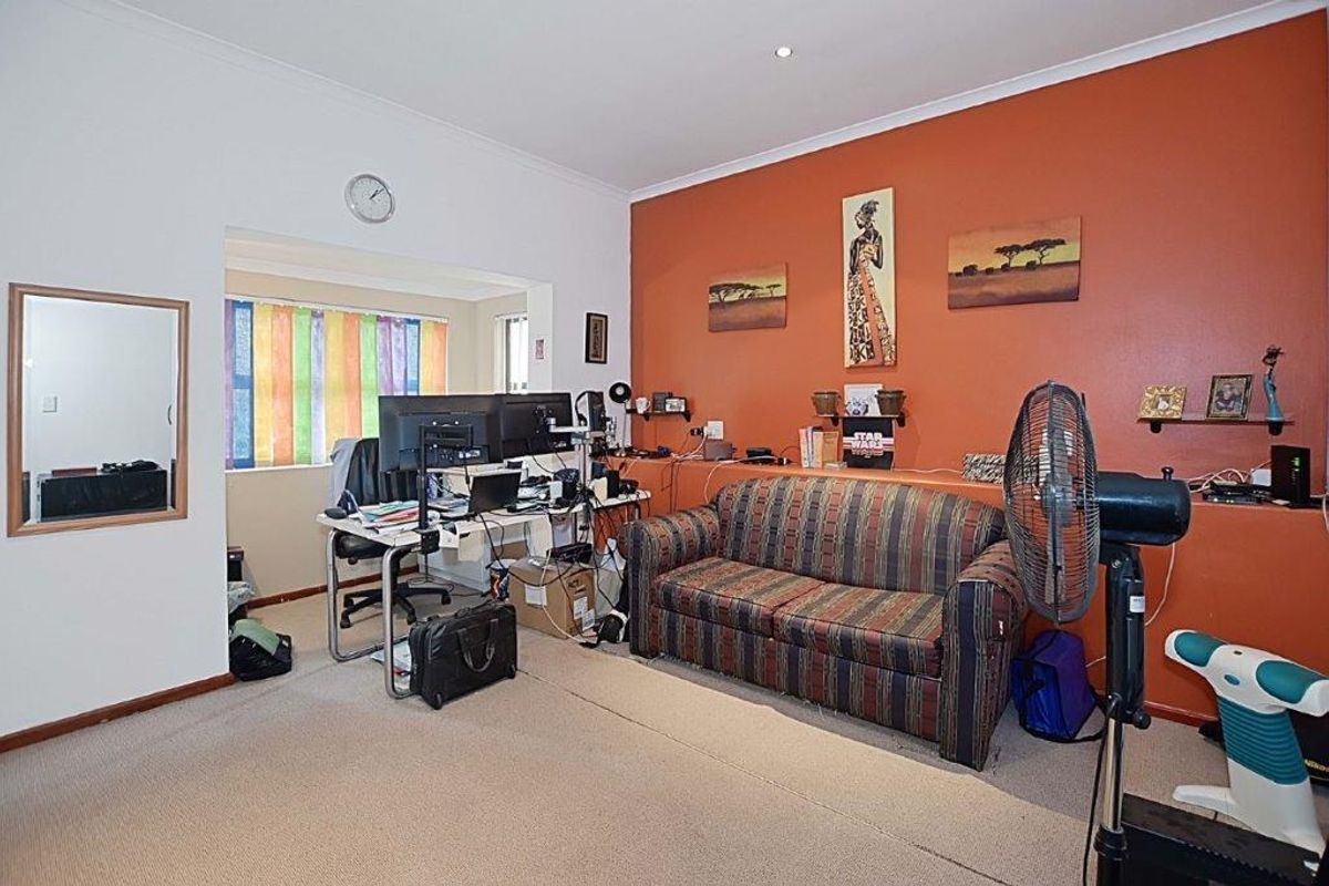 A living area featuring a prominent accent wall, neutral carpeting, and an adjoining alcove space suitable for a home office or study area.