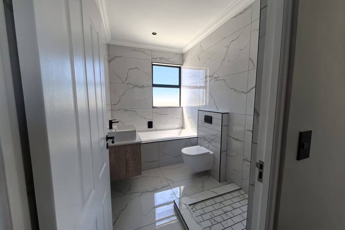 Modern bathroom featuring marble-look wall and floor tiles, a wall-mounted toilet, a built-in bathtub, and a contemporary vanity unit.