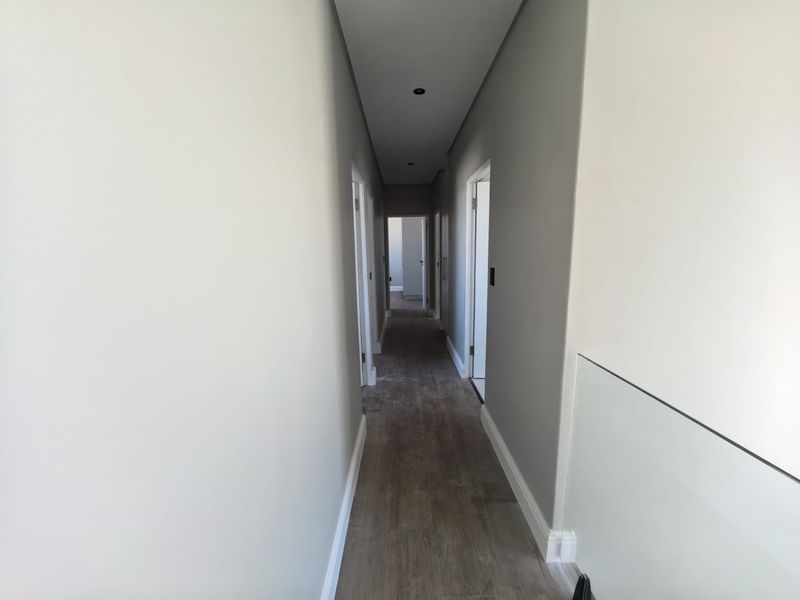 A clean, modern hallway featuring neutral grey walls, recessed ceiling lighting, and wood-look flooring, providing access to multiple rooms.