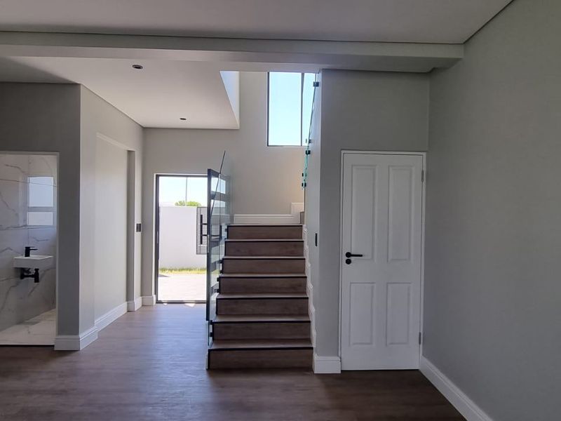 A bright, modern entrance hall featuring a staircase with glass balustrades, wood-look flooring, and access to a ground-floor bathroom.