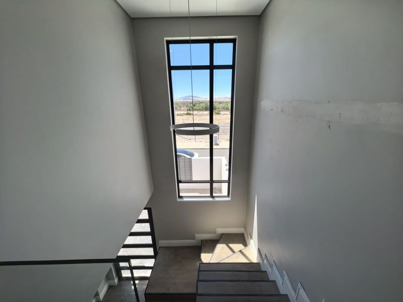 A bright staircase area featuring a tall, modern window with views, contemporary pendant lighting, and wood-look flooring.