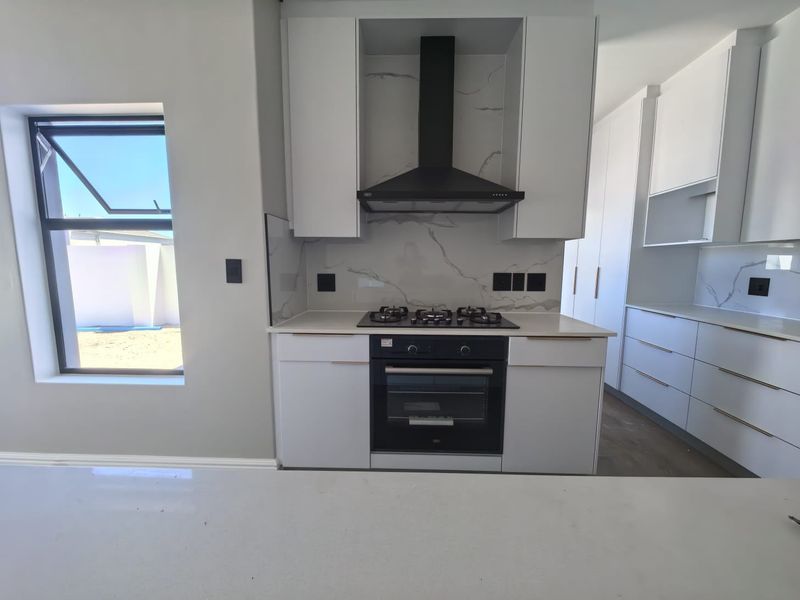Modern kitchen featuring white cabinetry, stone countertops, marble-look splashback, and integrated gas hob with extractor fan.