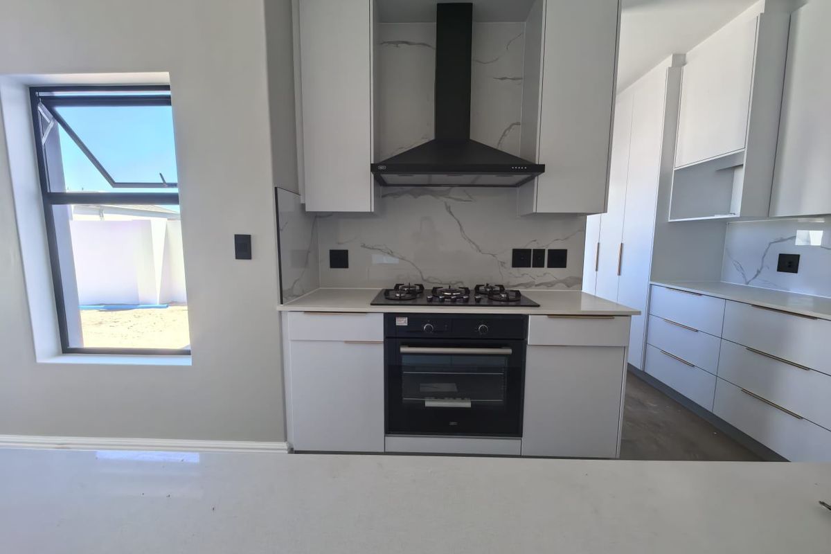 Modern kitchen featuring white cabinetry, stone countertops, marble-look splashback, and integrated gas hob with extractor fan.