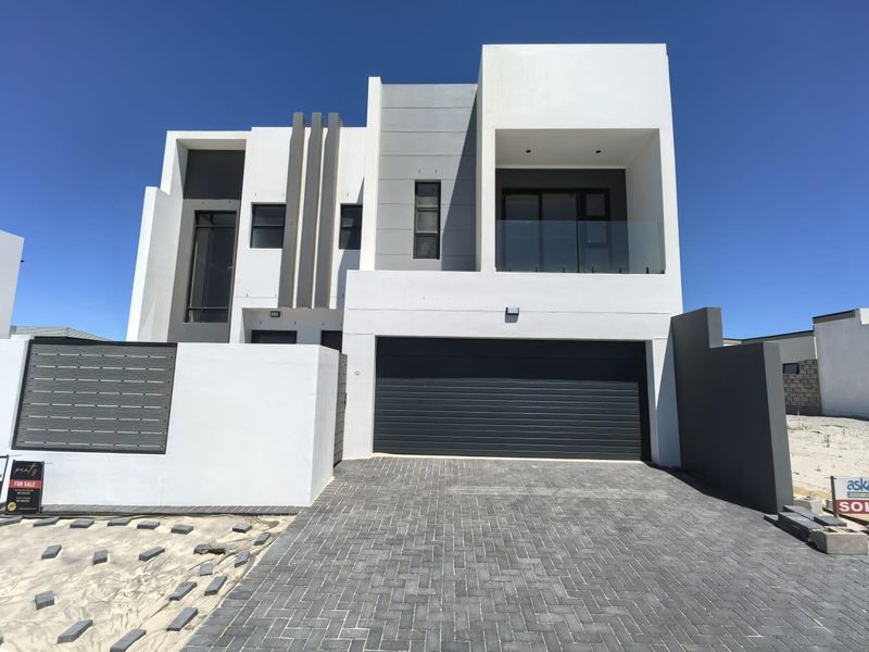 Modern double-story residential facade featuring a sleek contemporary design, paved driveway, integrated double garage, and an upper-level balcony with glass balustrading.
