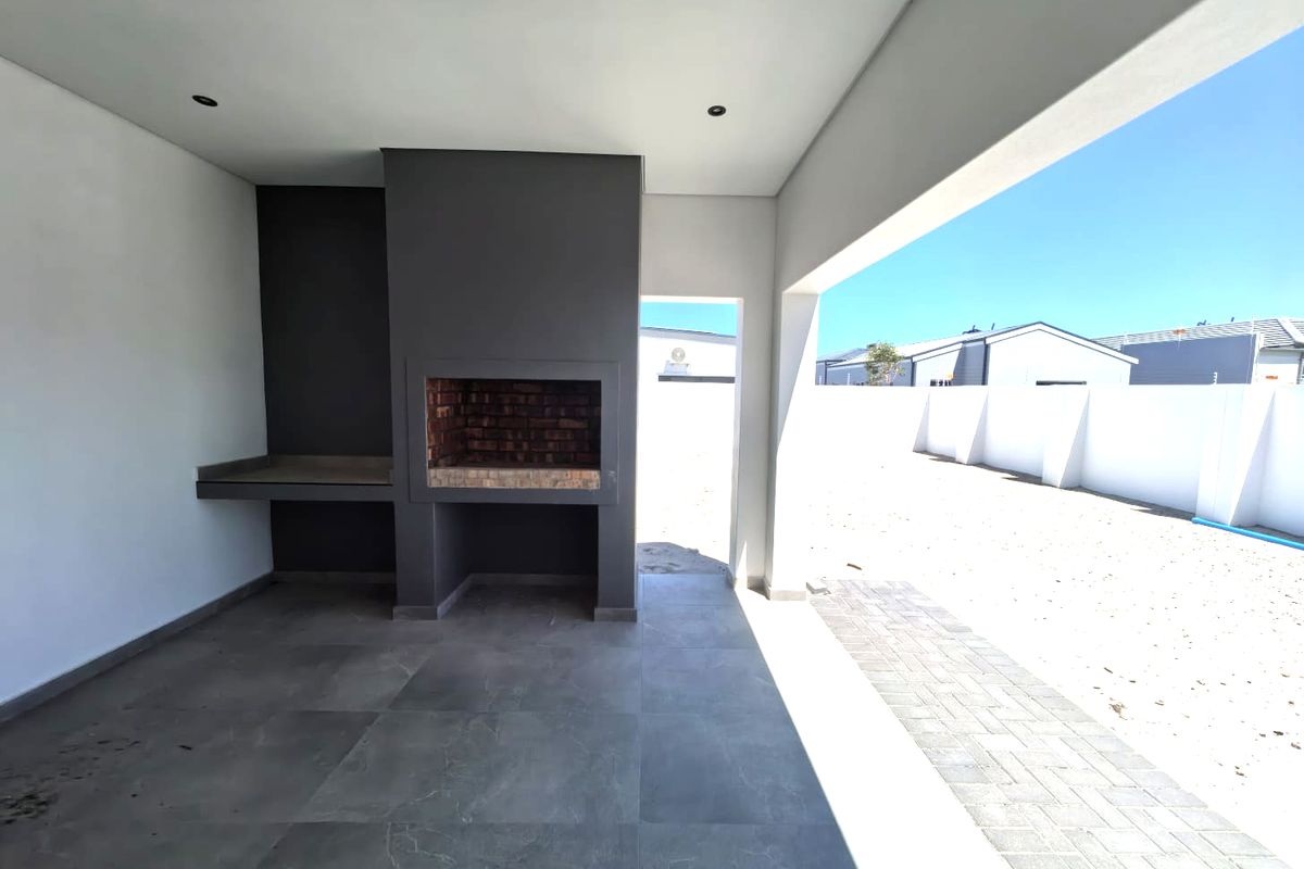 A covered patio area featuring a built-in brick braai and prep counter, overlooking an expansive, undeveloped backyard space.