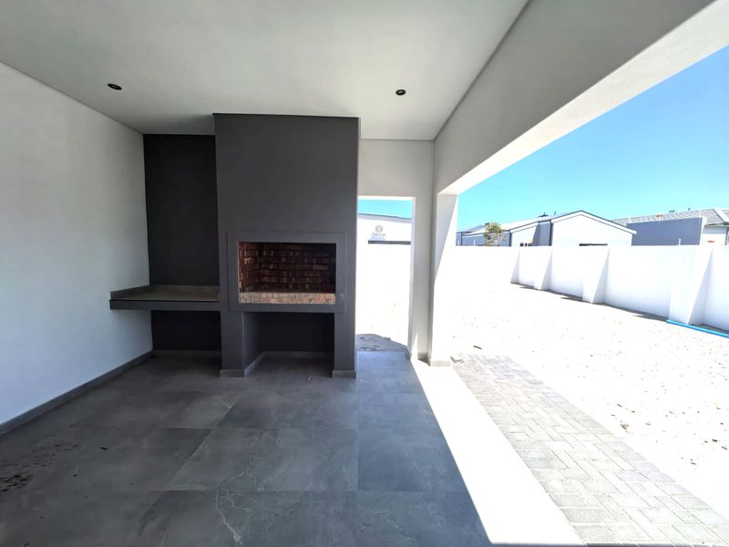 A covered patio area featuring a built-in brick braai and prep counter, overlooking an expansive, undeveloped backyard space.