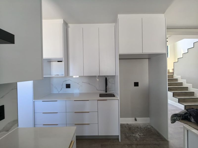 Modern kitchen scullery area featuring sleek white cabinetry, marble-look splashback, integrated sink, and dedicated space for appliances.